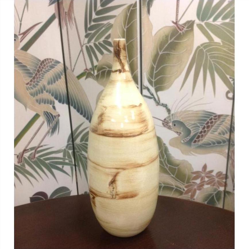 Two-tone beige and brown ceramic vase in front of nature-themed wallpaper with birds and leaves.