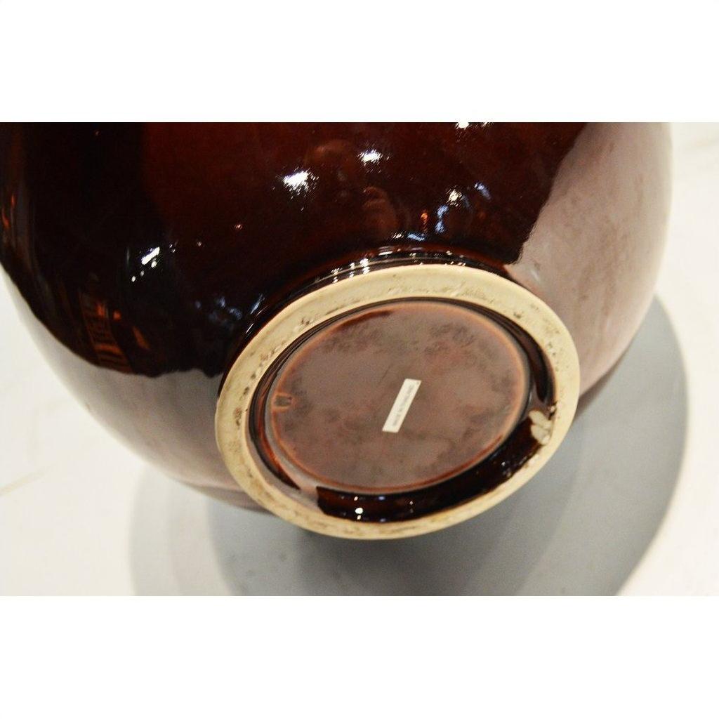 Close-up of glossy brown ceramic jar base with small white label, Prem Collection Artisan series.