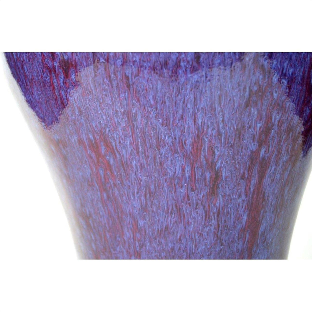 Close-up of purple, blue, and red glazed ceramic vase with textured surface on white background.