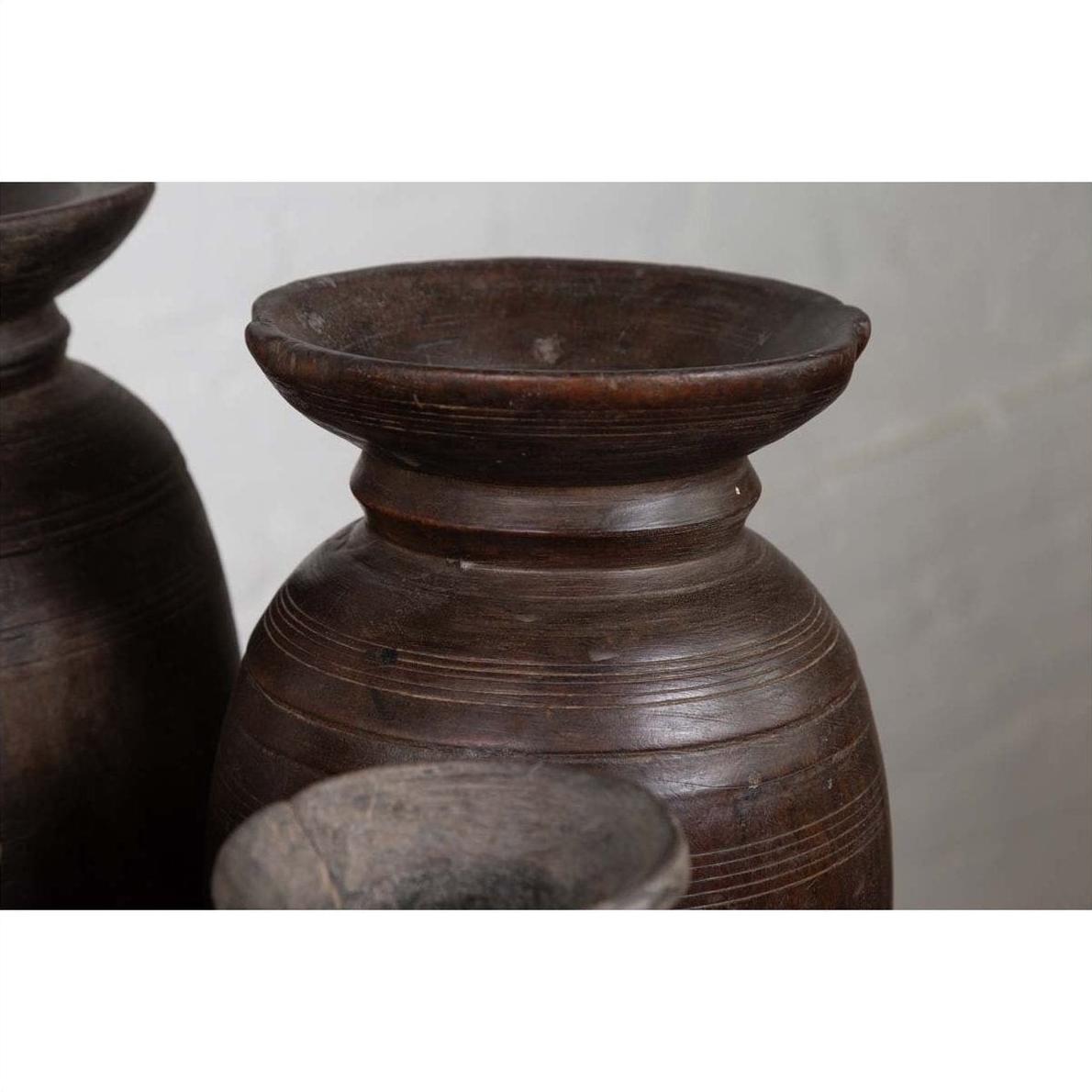 Close-up of brown wooden ghee pots with carved horizontal lines, rustic style, grouped together on a flat surface.