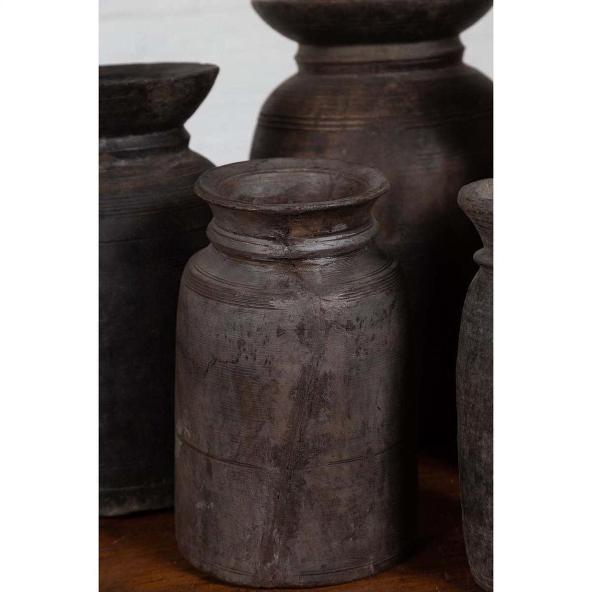 Brown wooden ghee pots in groups of three, five, or seven displayed with clay pots on a wooden surface.