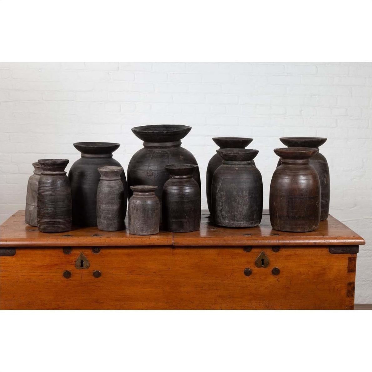Brown wooden ghee pots in varying sizes on a chest, set against a white brick wall, rustic style.