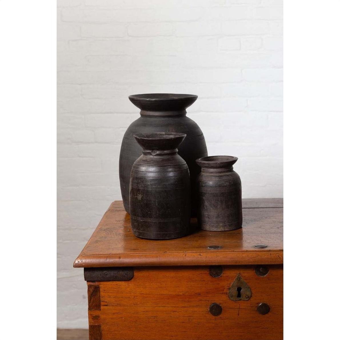 Brown wooden ghee pots on wooden chest, white brick wall background, rustic Nepalese style, indoors.