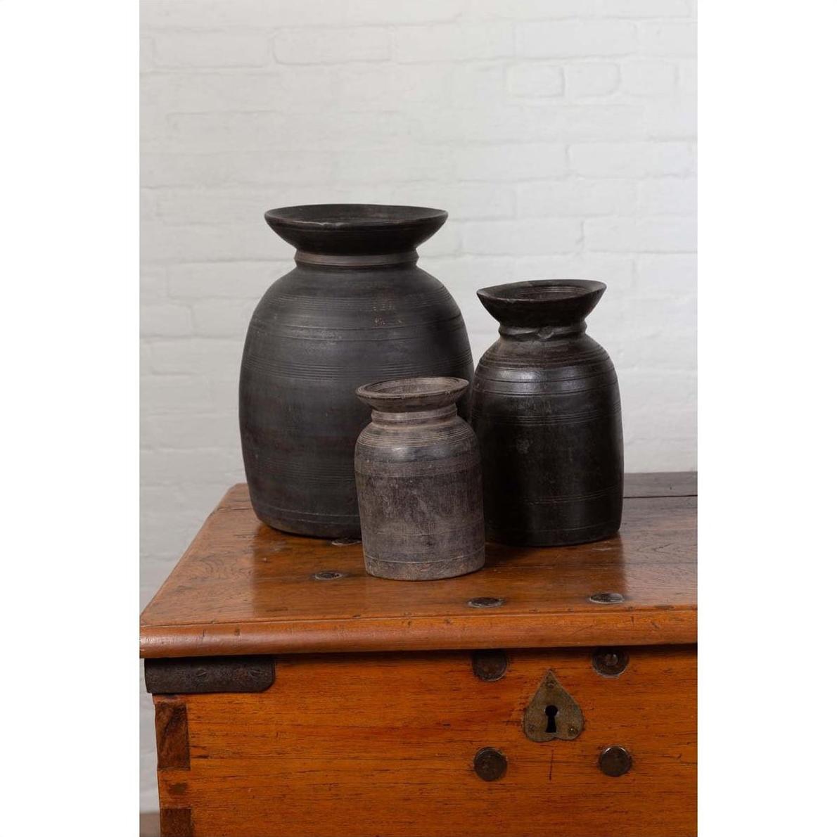 Brown wooden ghee pots on a chest against a white brick wall indoors.