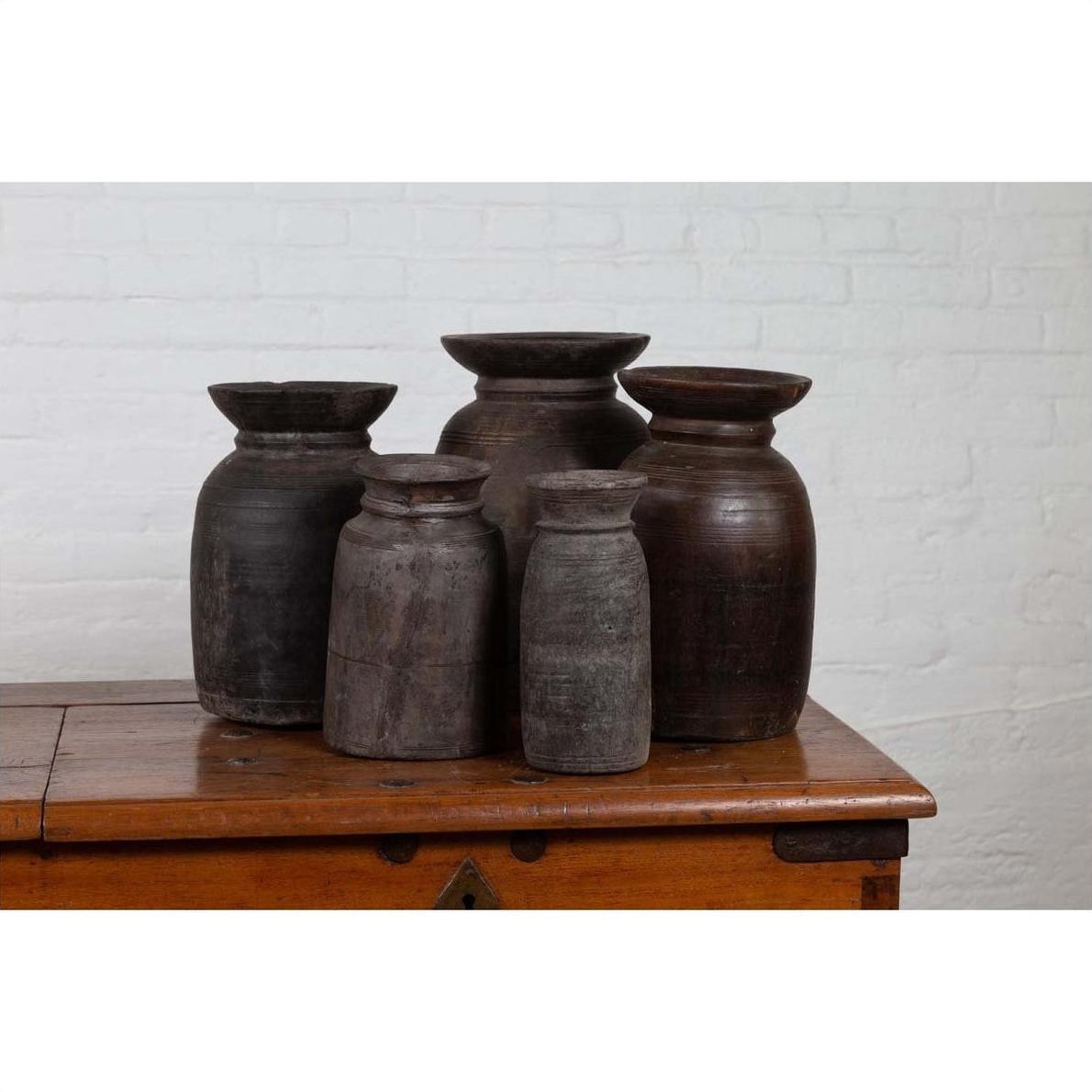 Brown wooden ghee pots set of five on a wooden chest, white brick wall background, indoors.