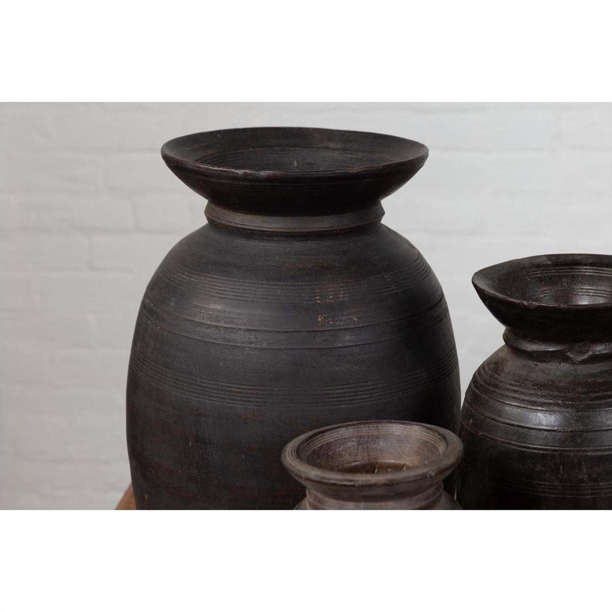 Brown wooden ghee pots in a rustic style, grouped together against a light brick wall.