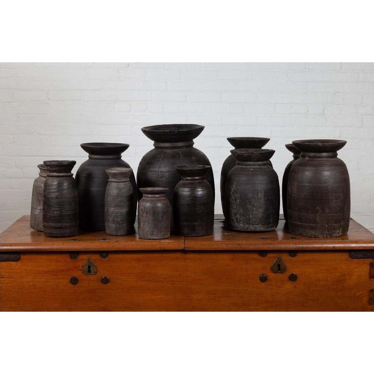 Brown rustic wooden ghee pots in groups of 3, 5, and 7 against a white brick wall indoors.