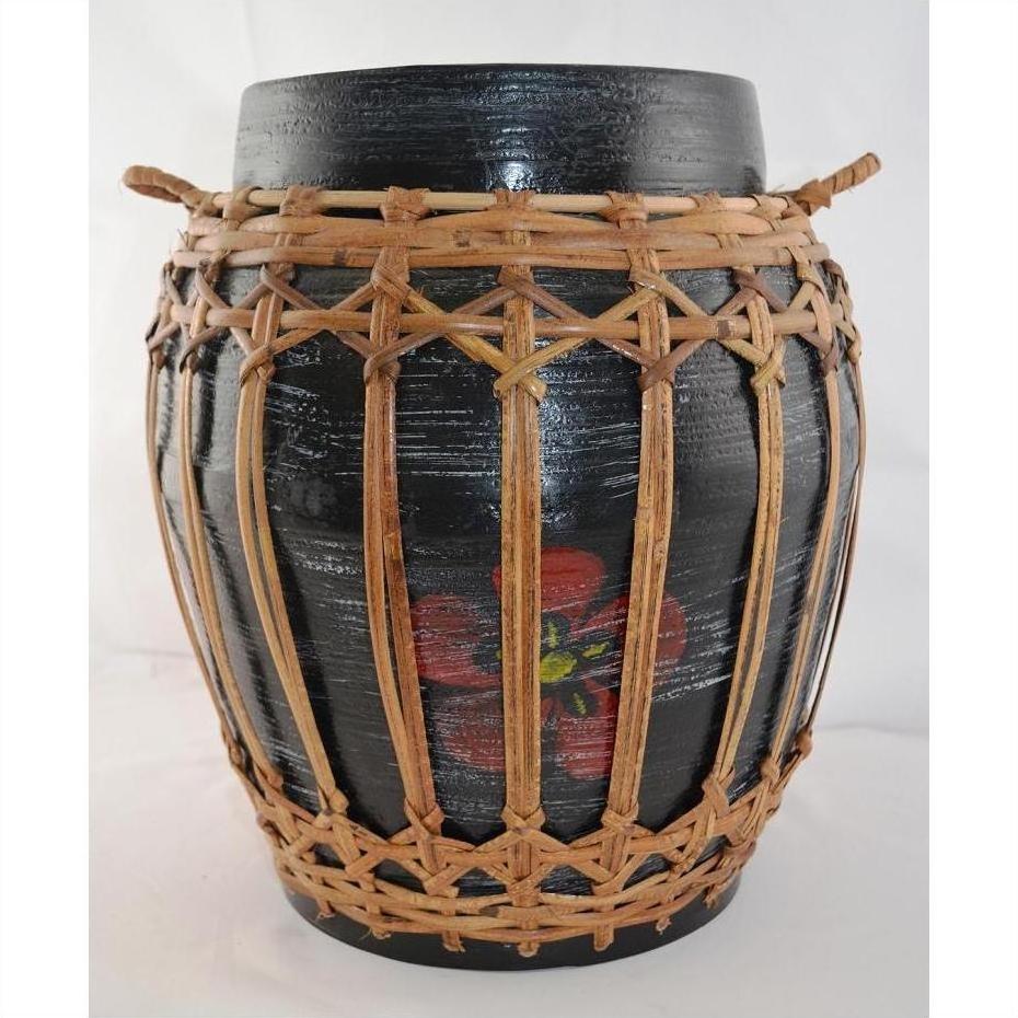 Close-up of a black ceramic jar with red flower design in a rattan and bamboo lidded basket with handles.