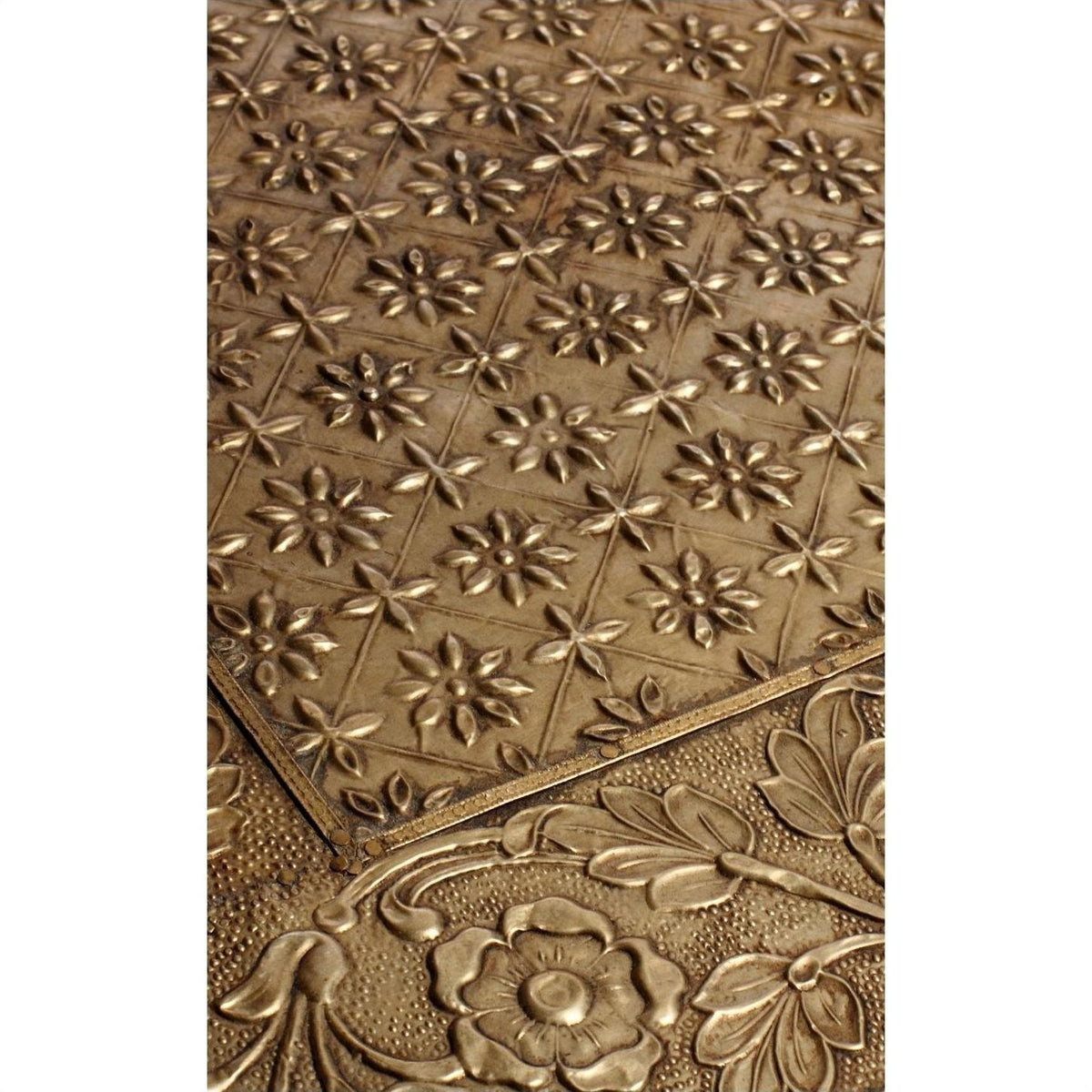 Close-up of silver hammered metal tiles with floral and geometric patterns overlapping on a small rectangular table.