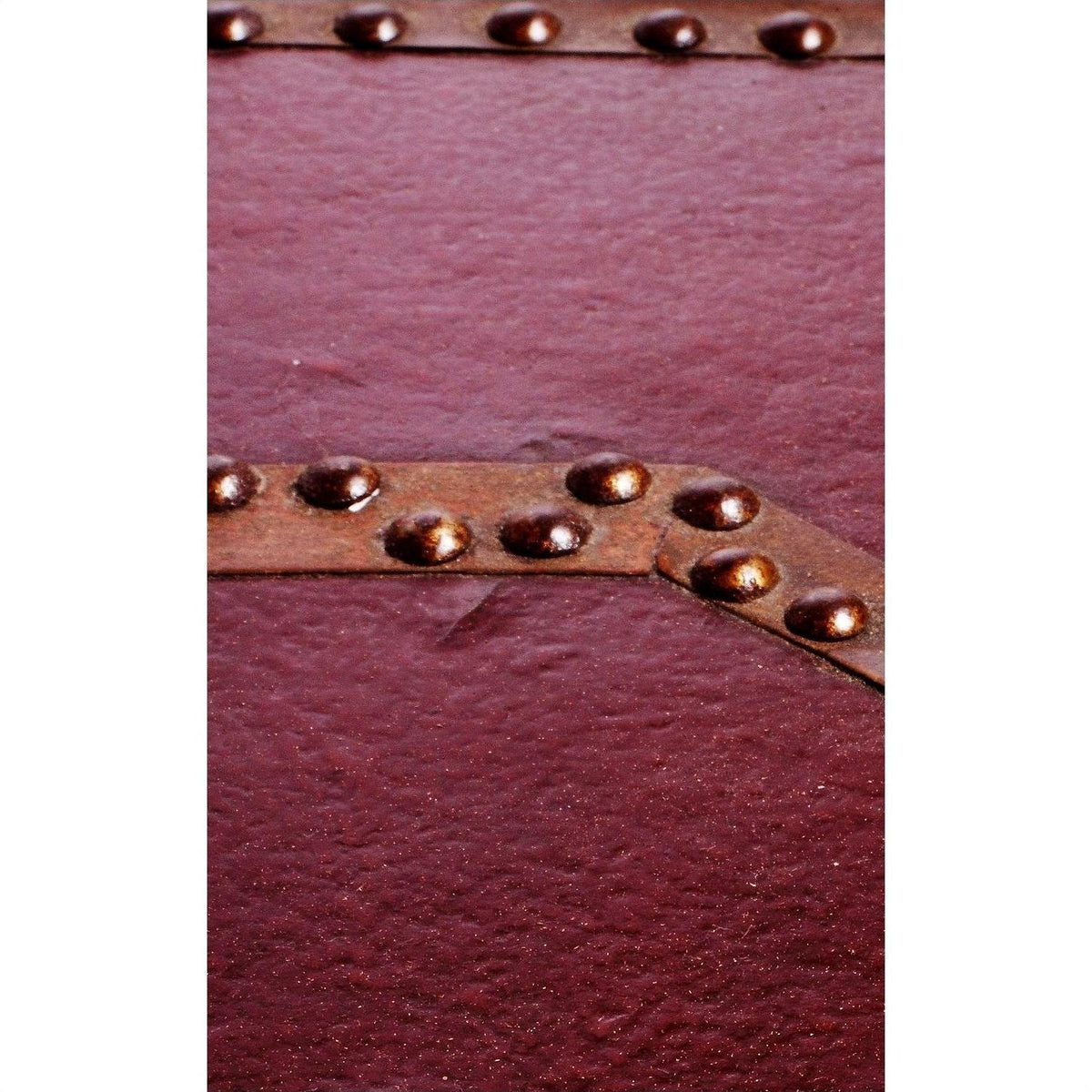 Close-up of maroon red lacquer trunk with textured finish and diagonal brass-studded metal strip.