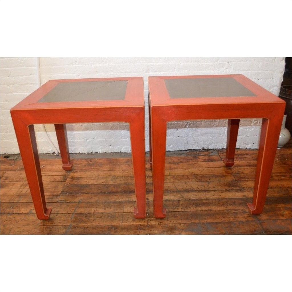 Red side tables with inset floor tiles, set on a wooden floor in front of a white brick wall.