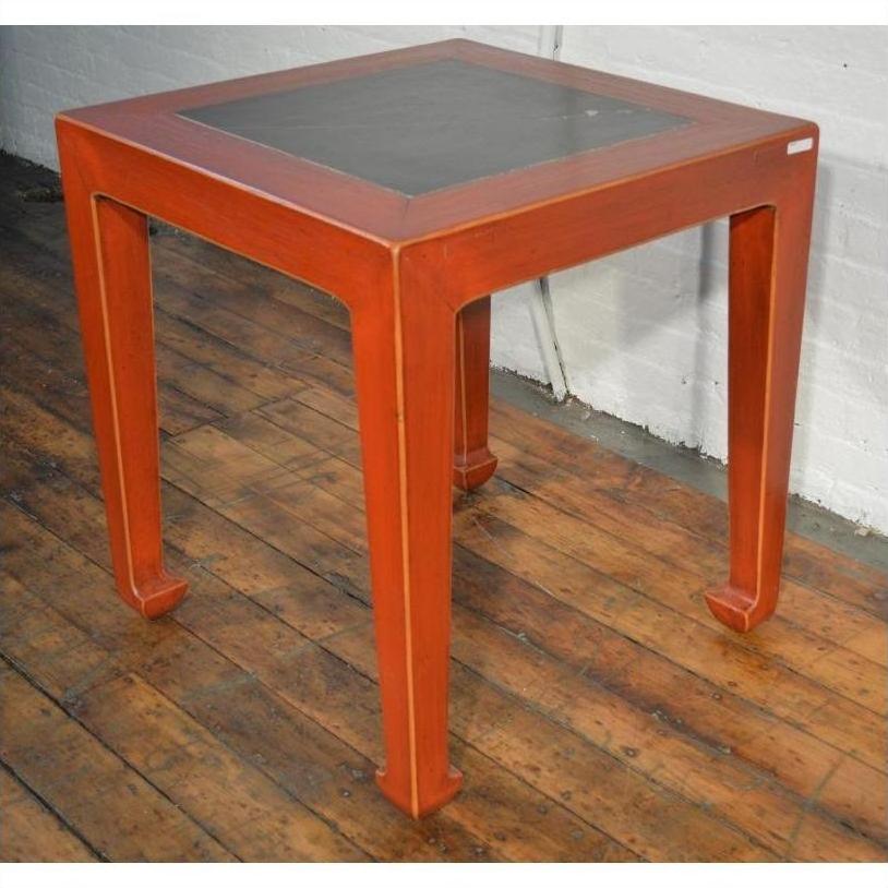 Red side tables with inset floor tiles on wood flooring next to a white brick wall, styled interior setting.