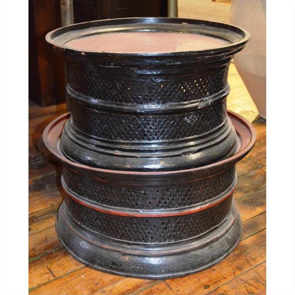 Round offering trays on a wooden floor next to a black lattice-patterned stool or drum.