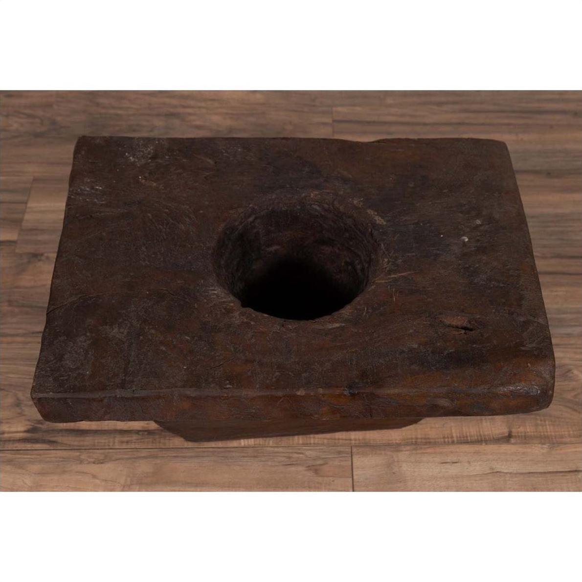 Brown wooden Indonesian planter with large circular hole, rustic design, on wooden floor indoors.