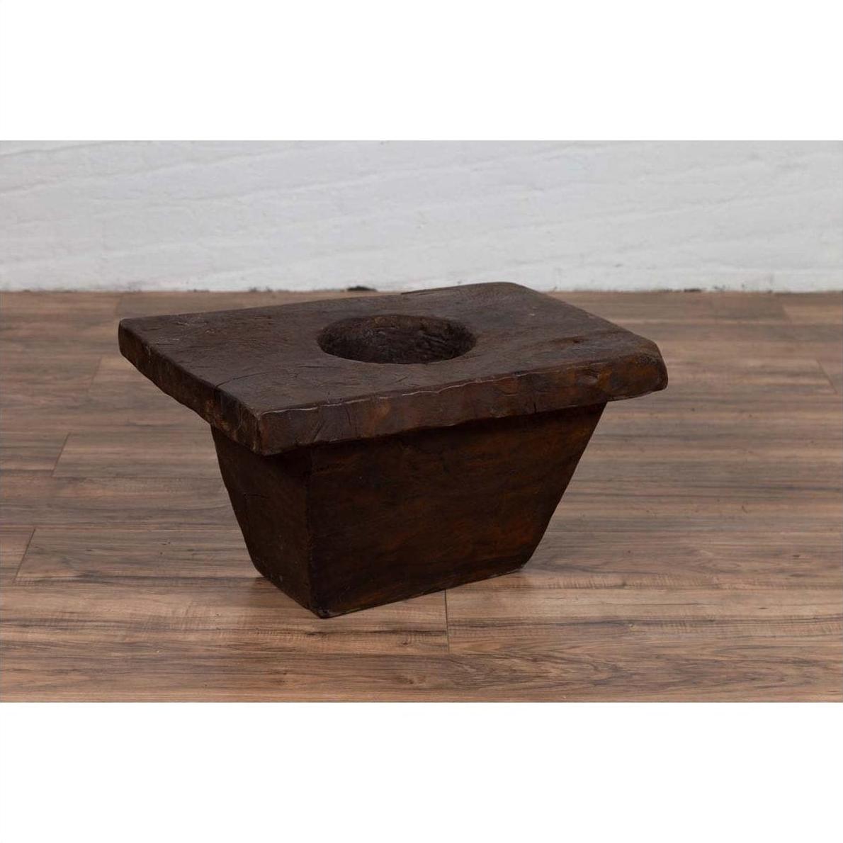 Brown wooden planter on wooden floor next to a white brick wall, rustic and antique style, early 20th century.