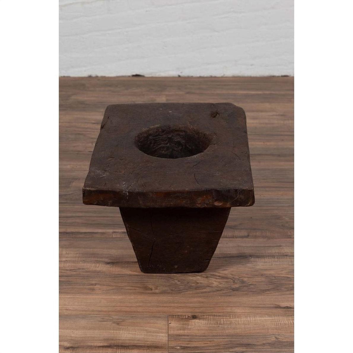 Brown wooden planter with large circular hole, antique Indonesian, early 20th century, on wooden floor indoors.