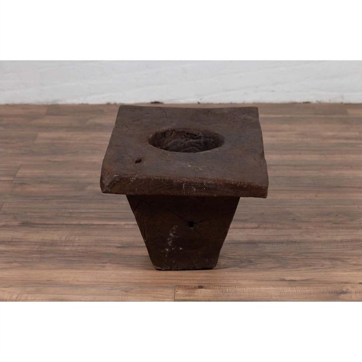 Brown wooden planter, antique Indonesian style, on a wooden floor beside a white wall indoors.