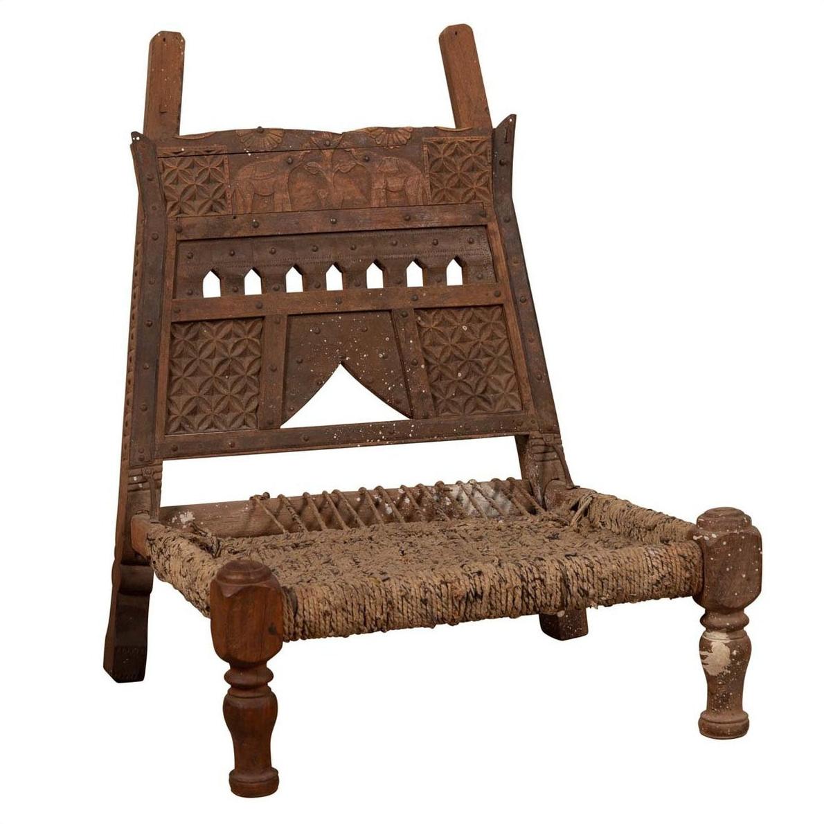 Brown wooden chair with rope seat, carved backrest, weathered finish, antique style, shown indoors.