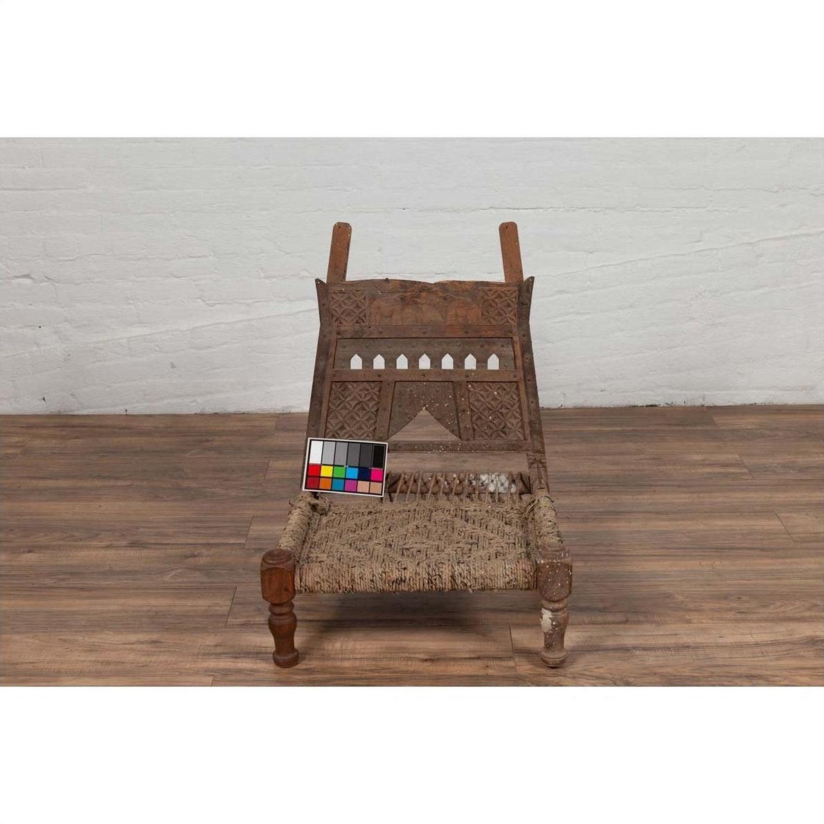 Brown wooden low chair with rope seat and weathered finish on a wooden floor indoors.