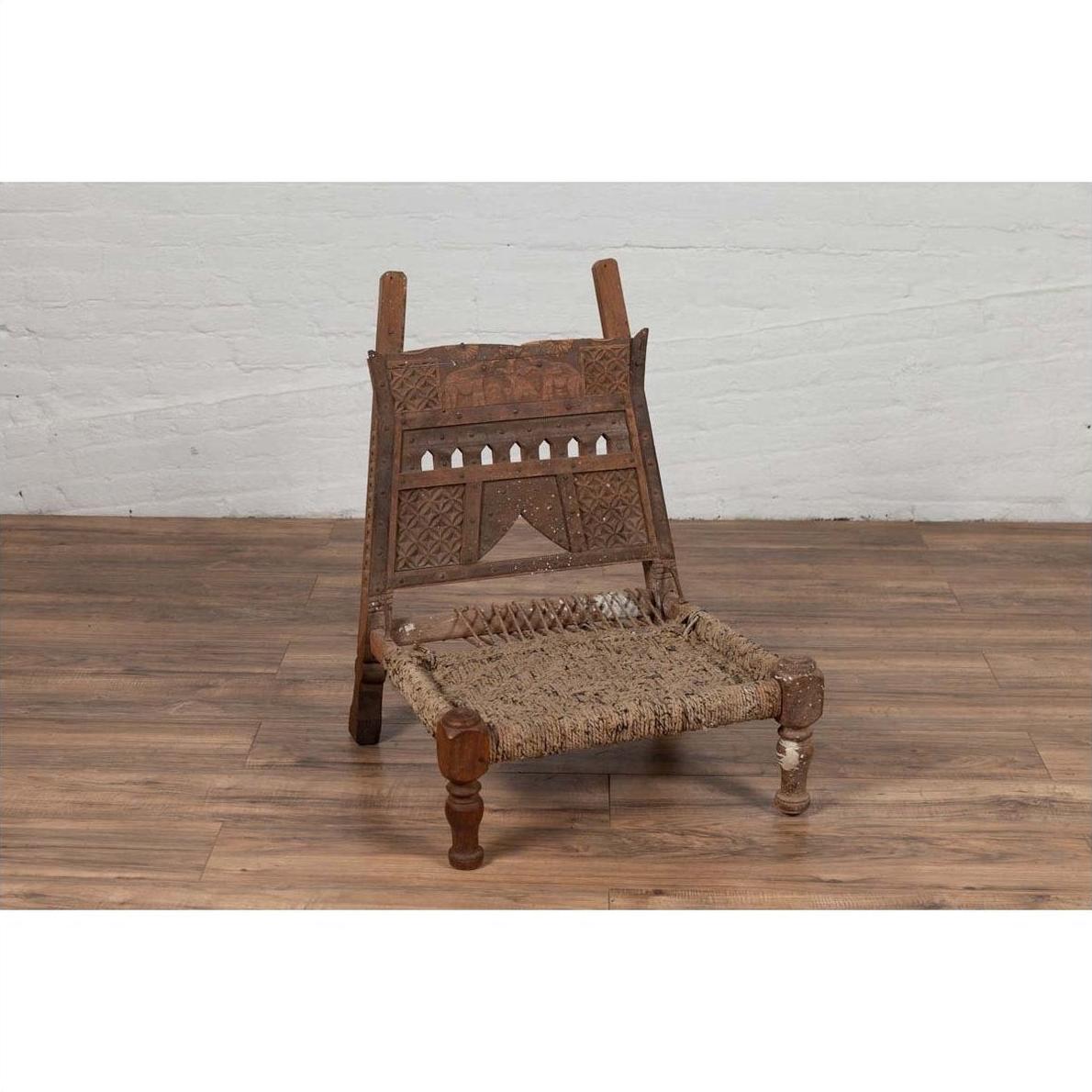 Brown wooden chair with rope seat and weathered finish on wooden floor against white wall indoors.