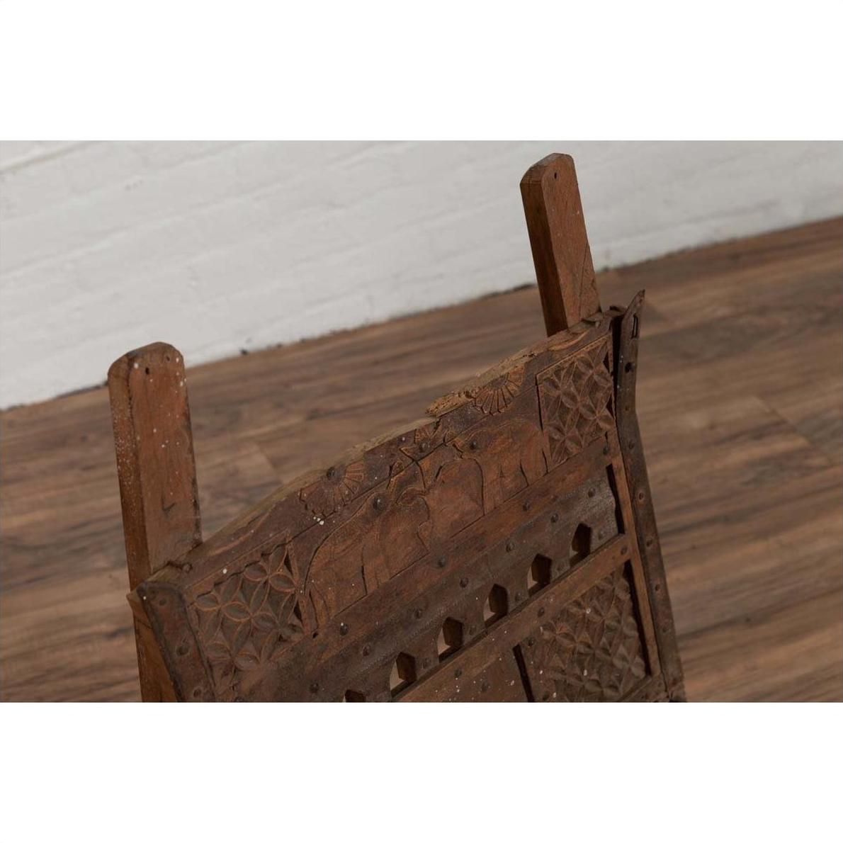 Close-up of brown wooden chair with rope seat, weathered finish, on wood floor next to a white brick wall indoors.