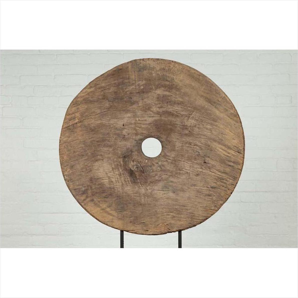 Brown wooden ox cart wheel on black base against white brick wall indoors.