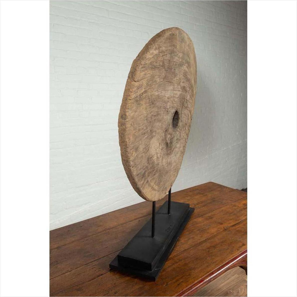 Brown wooden ox cart wheel with black painted base displayed on a wooden table.