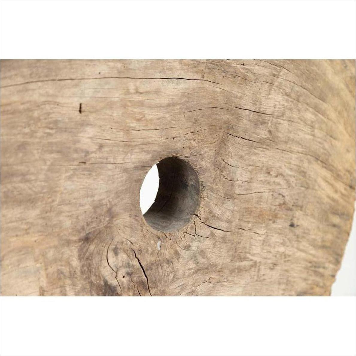 Close-up of brown weathered wooden ox cart wheel from Thailand on black painted base, showing grain and central hole.