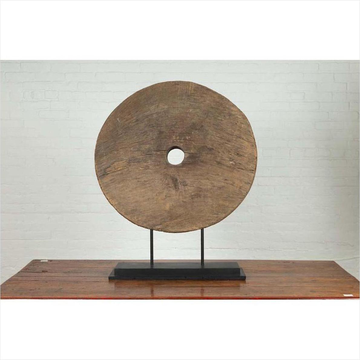 Brown wooden ox cart wheel from Thailand on a black painted base, displayed as decor.