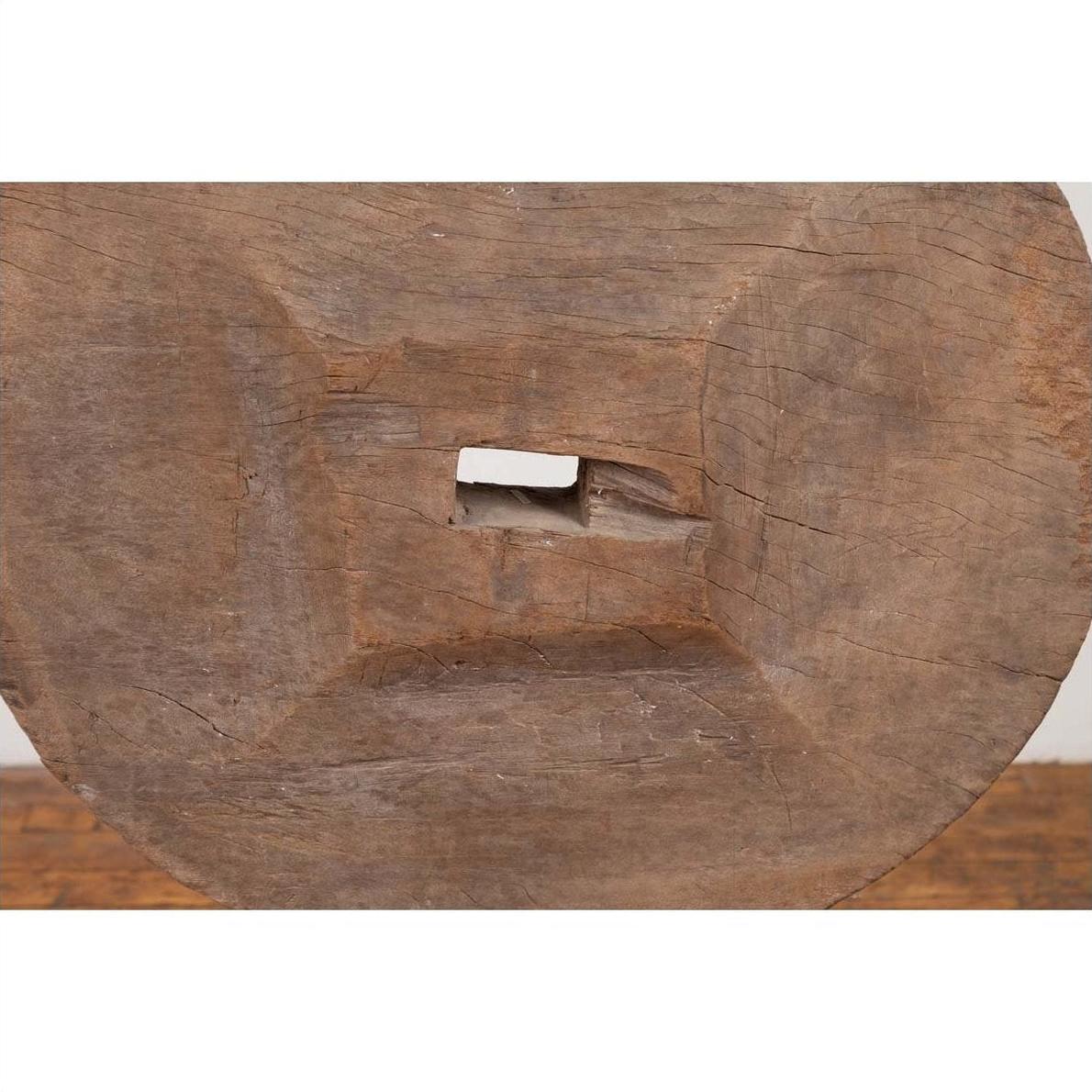 Close-up of a brown wooden ox cart wheel from Thailand on a black painted base.