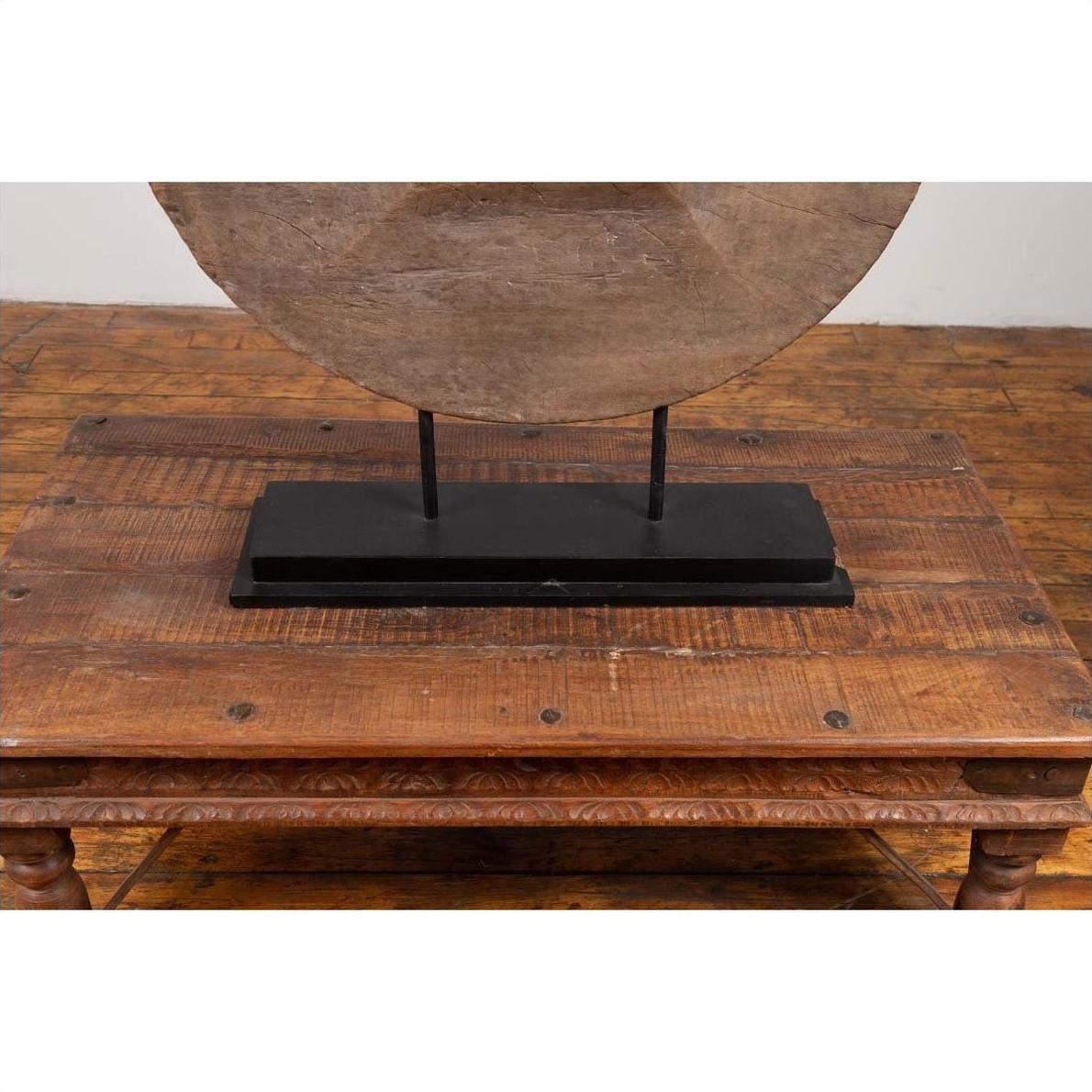 Brown wooden ox cart wheel on black painted base, displayed on a wooden table.