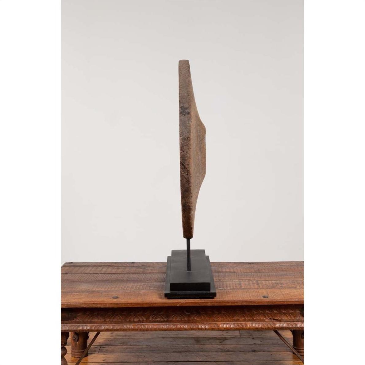 Brown wooden ox cart wheel from Thailand on black base, with rustic decor, displayed on a wooden table.