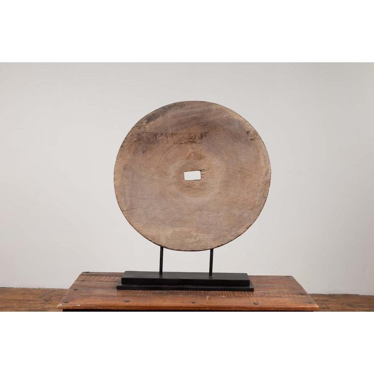 Brown wood ox cart wheel, 19th century Thailand, mounted on black painted base, upright display.