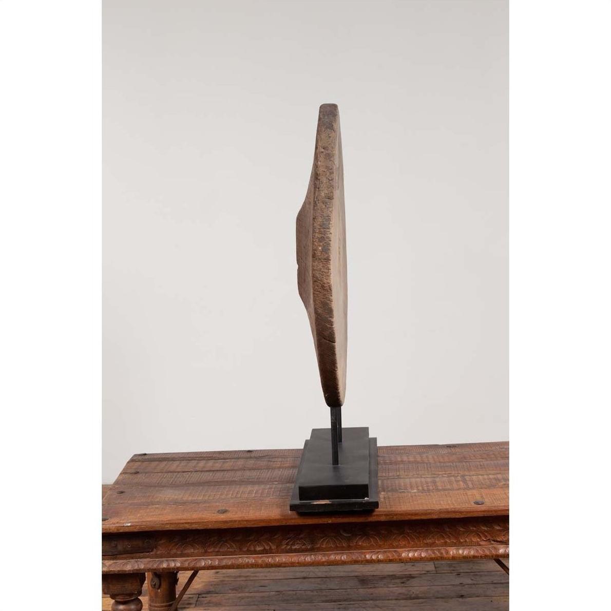 Brown wooden ox cart wheel from Thailand on black base, displayed on wooden table, plain background.