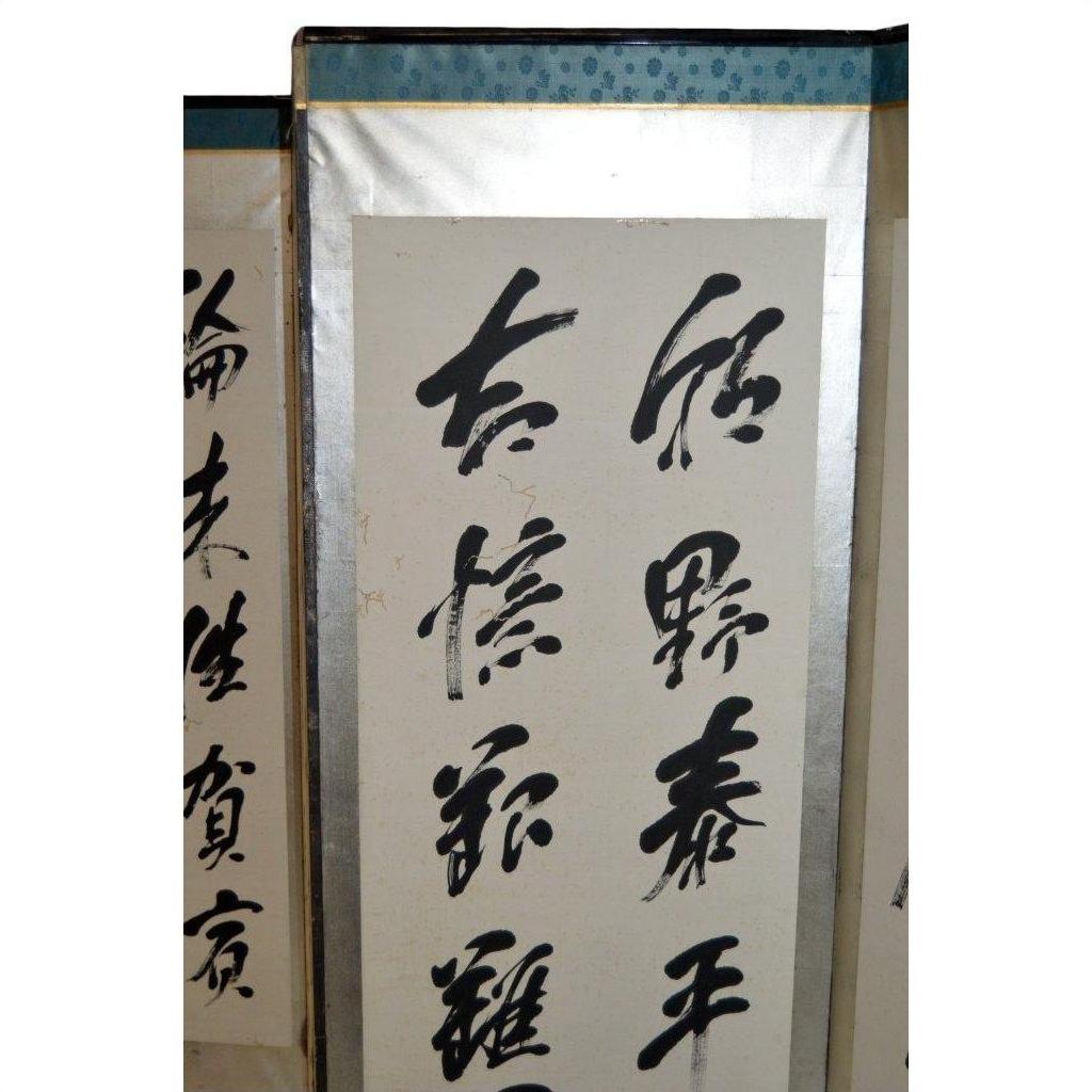 Black Chinese calligraphy on vertical scroll with silver frame, overlapping 6-panel Japanese calligraphy screen.