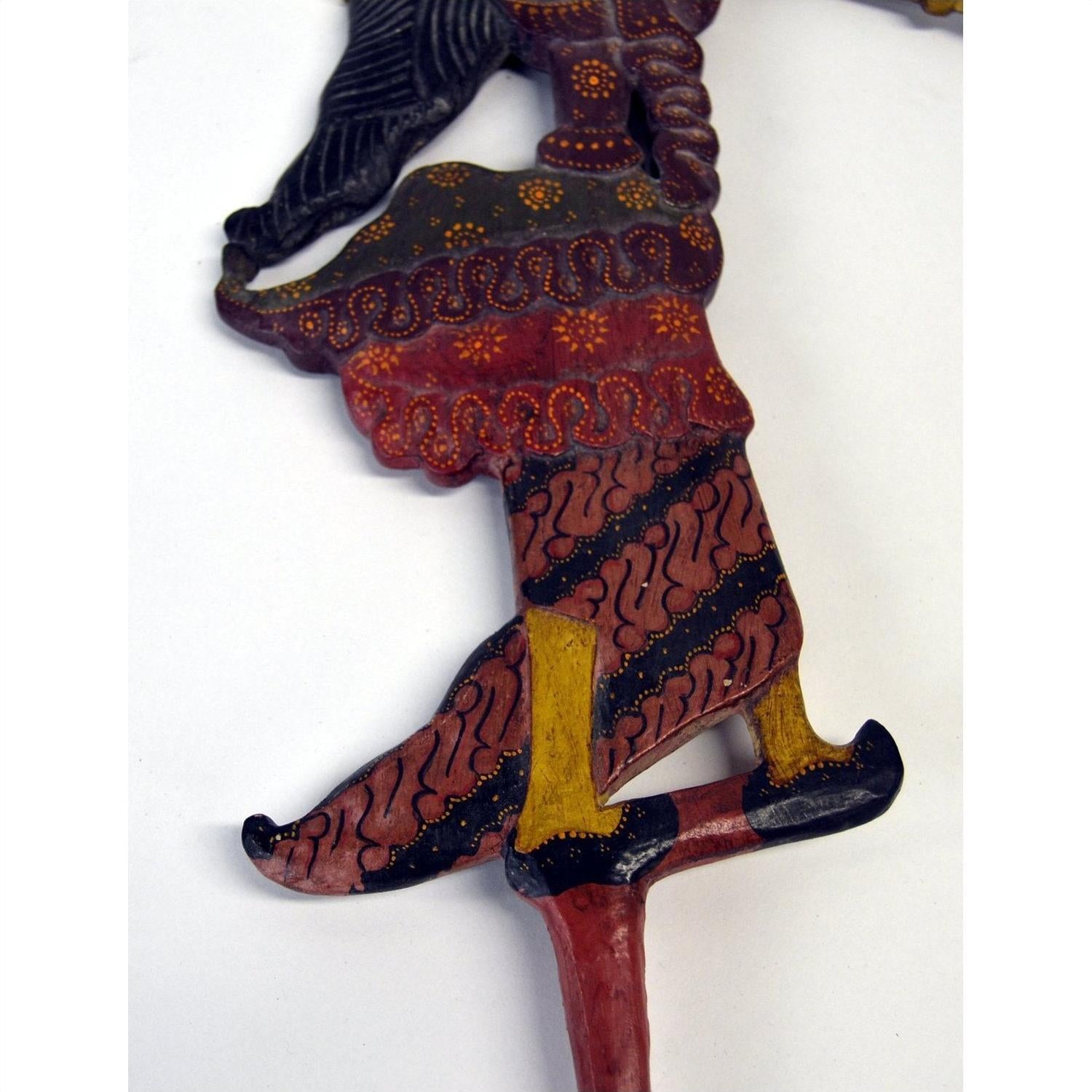 Close-up of brown wooden Wayang Kulit shadow puppets, focus on leg with curly-toed shoe.