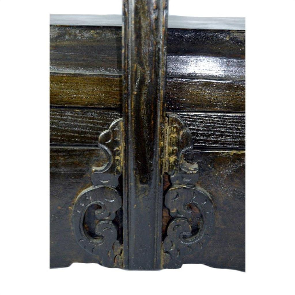 Close-up of dark wood elm box with ornate carved scrollwork and central beam detail.