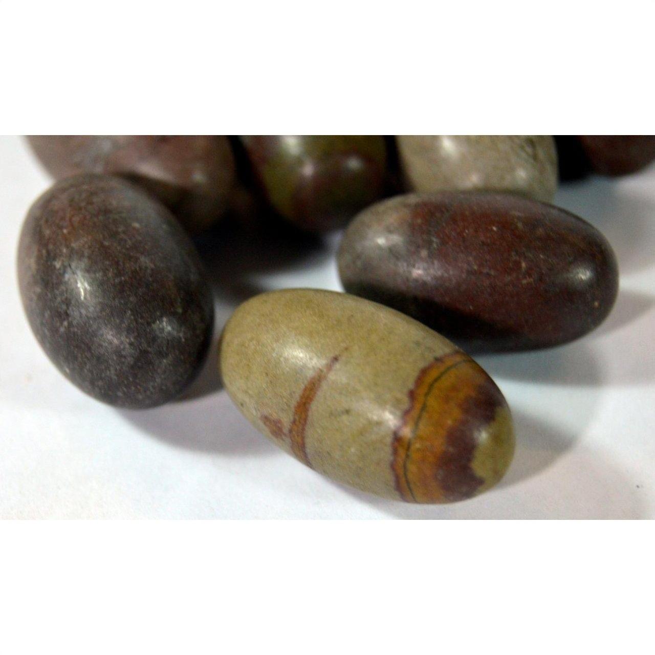 Brown and gray oval Shiva Lingam fertility stones with natural stripes, smooth texture, on white surface, close-up.
