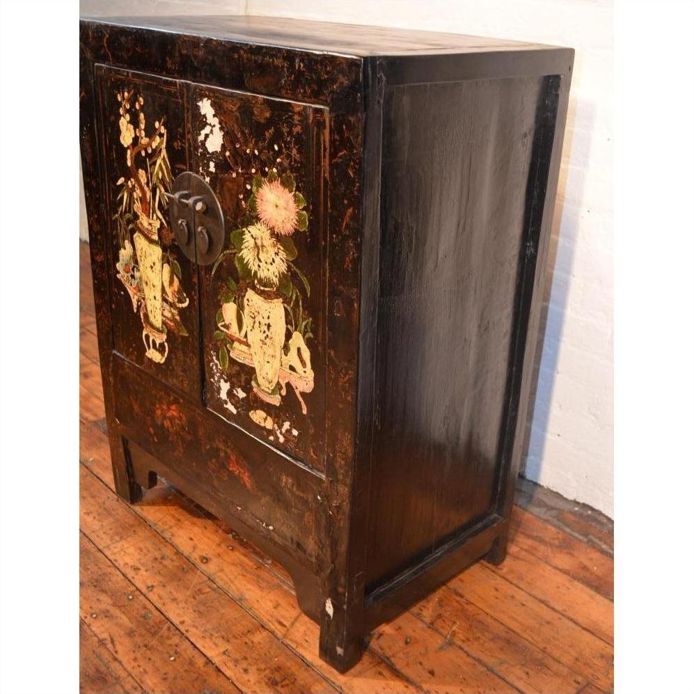 Wooden side cabinet with floral motif decoration and metal handle, displayed on a wooden floor.