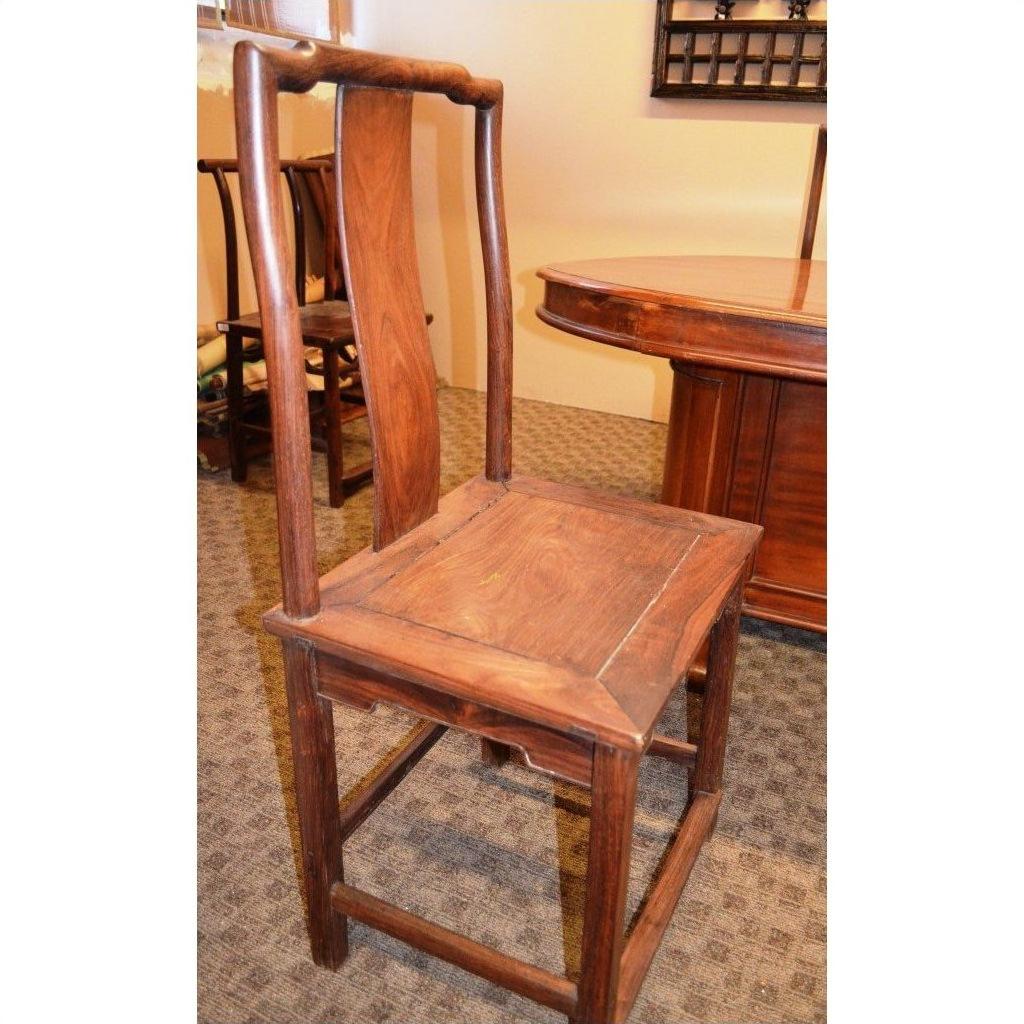 Brown wooden side chair with tall, curved backrest and square seat near a table on a carpeted floor.