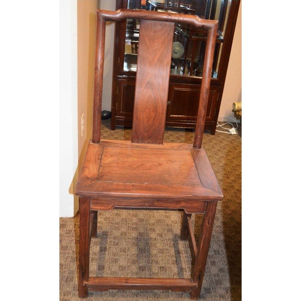 Brown wood side chair with tall curved backrest and square seat, next to a cabinet on a carpeted floor.