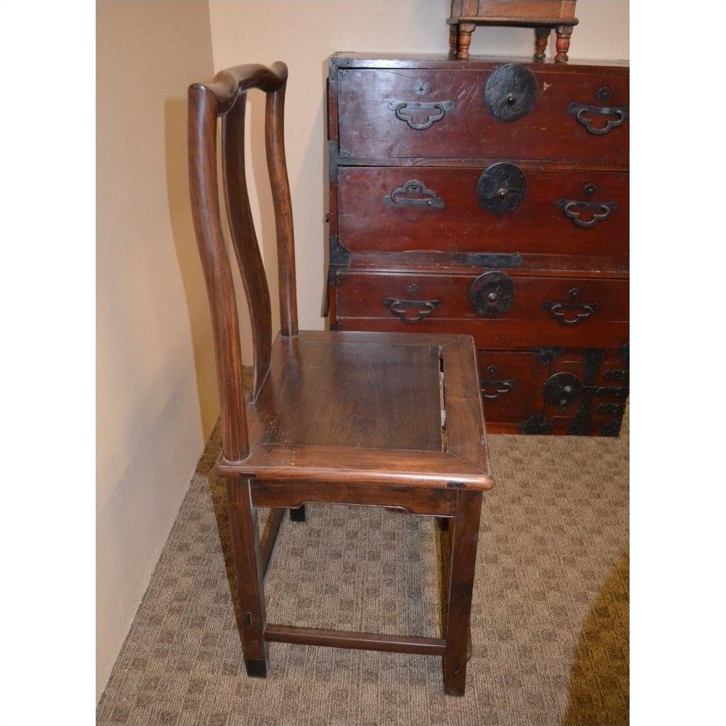 Brown wood side chair with curved backrest beside a vintage red wood chest with black metal handles and locks.