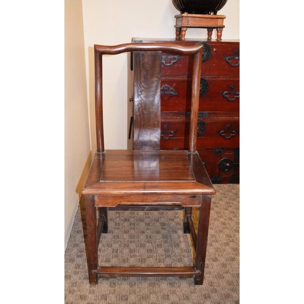Brown wooden side chair with straight backrest and curved top on a carpet next to a wooden chest.