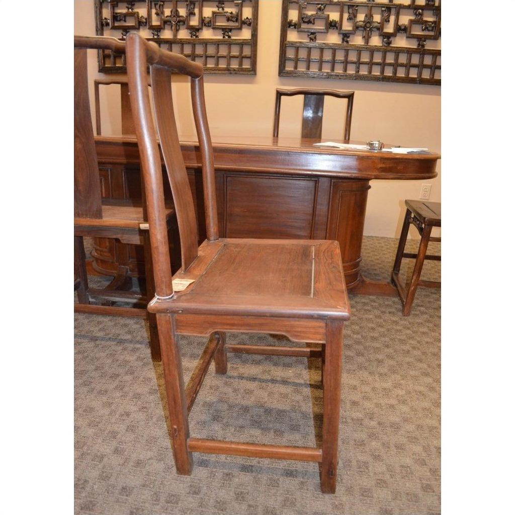 Brown wood side chair with straight backrest next to a table and other chairs in a carpeted room.