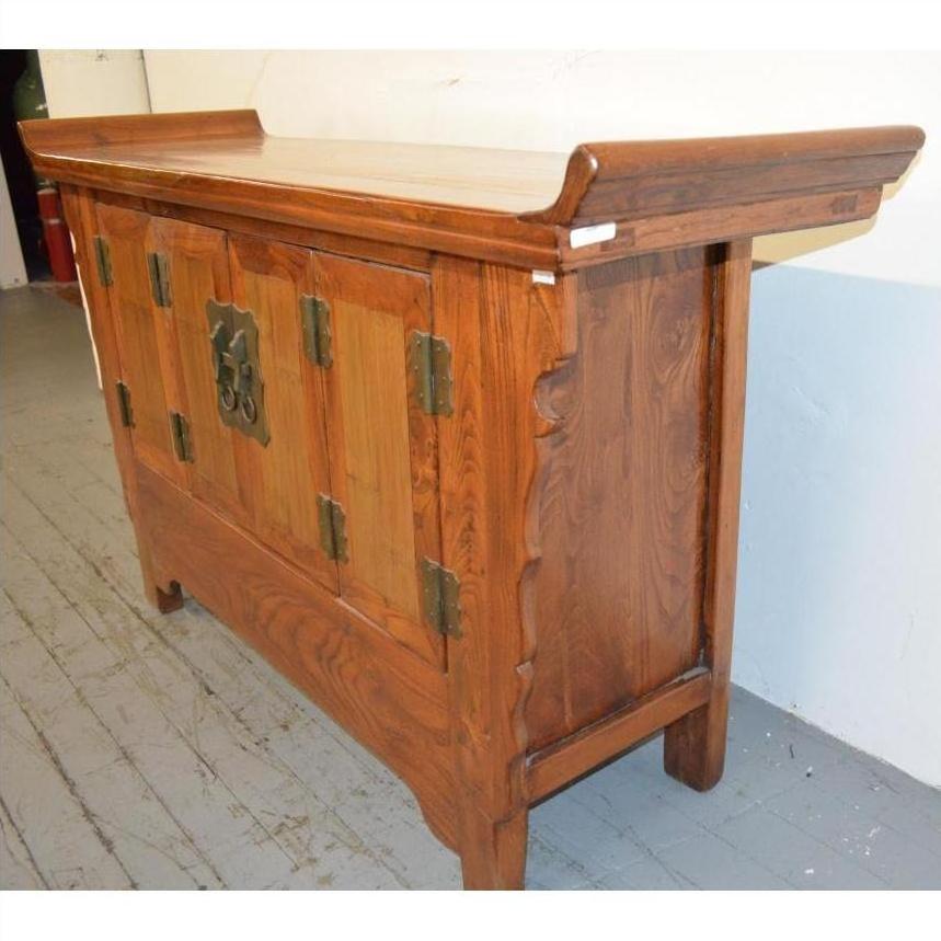 Gray wood sideboard with everted flanges and ornate metal handles, placed on a gray floor against a white wall.