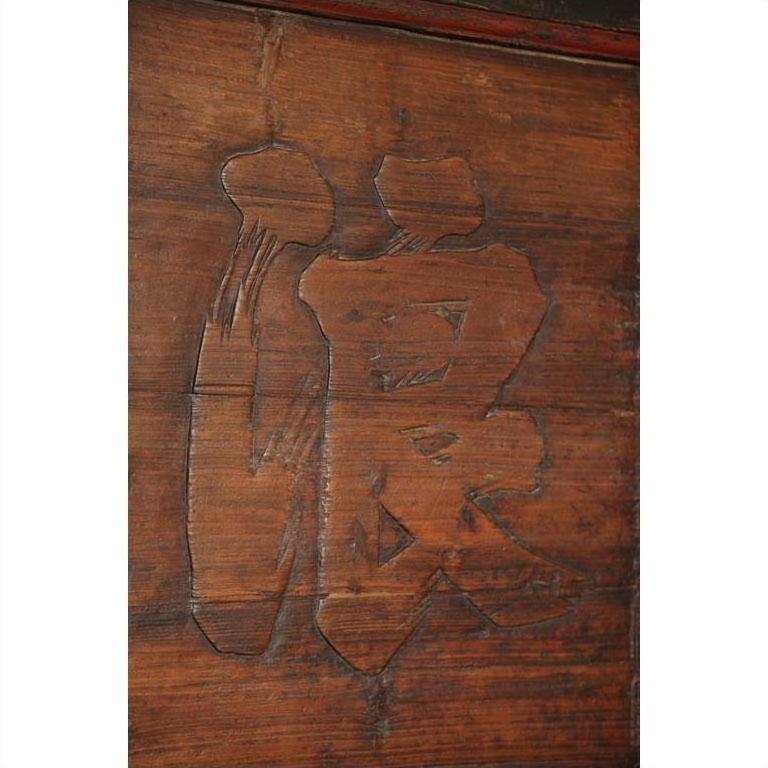 Close-up of a rustic wooden signboard with carved Chinese character, featuring textured brown wood surface.