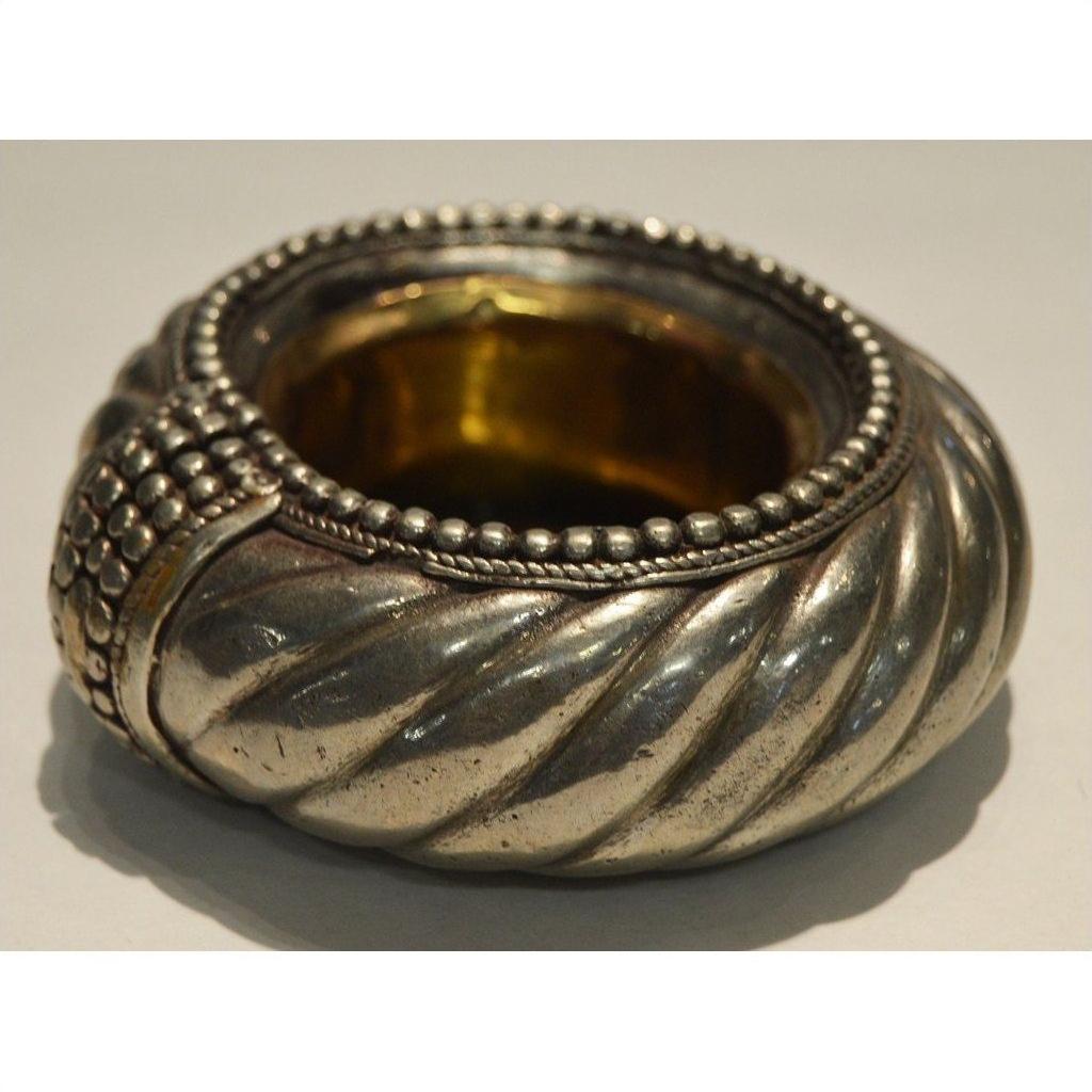 Close-up of a silver and brass dancer bracelet wine holder with twisted, beaded design on a plain surface.