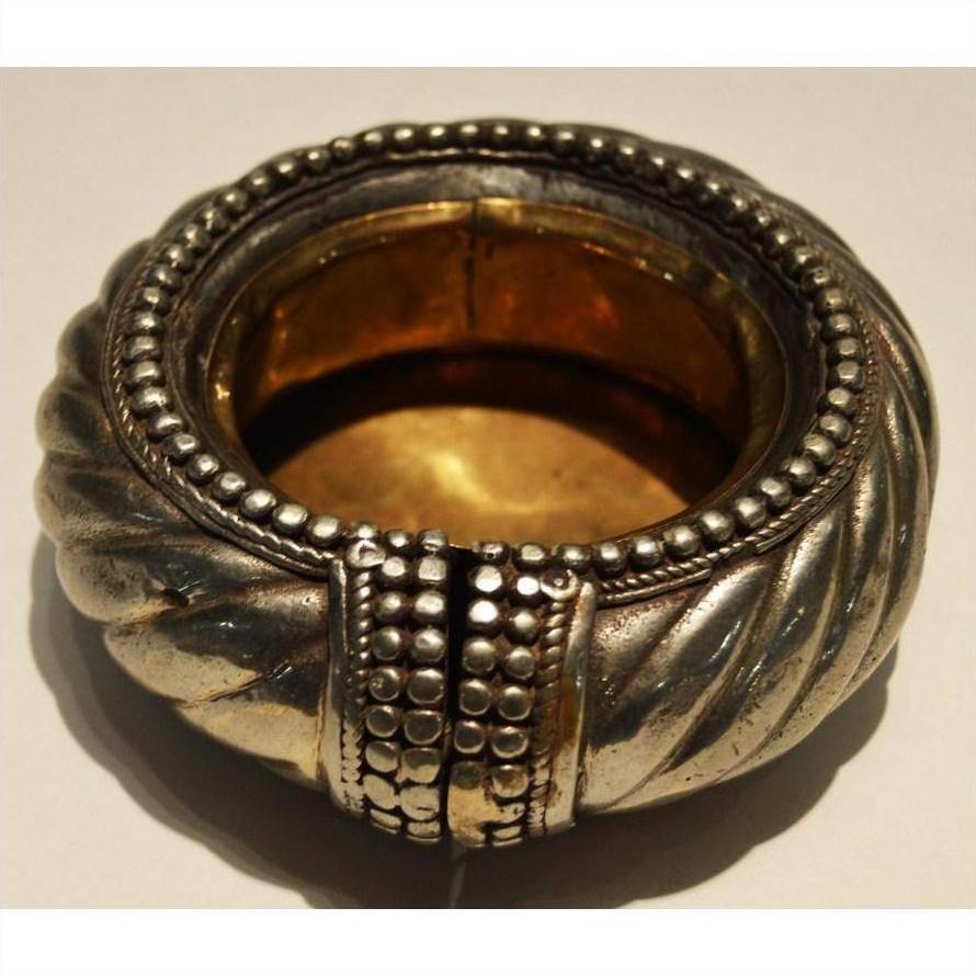 Close-up of silver and brass bracelet-style wine holder with ornate beaded and twisted patterns, gold and silver tones.