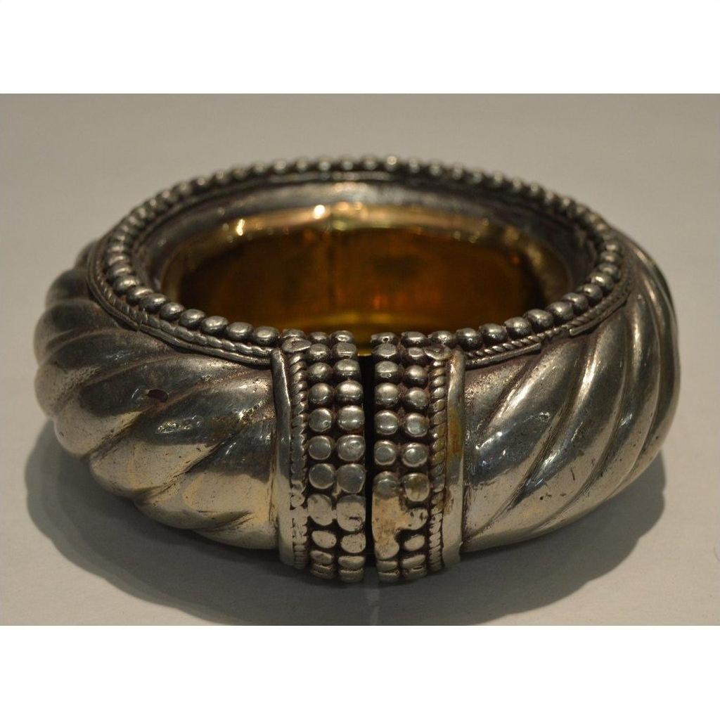 Close-up of a silver and brass twisted metal dancer bracelet wine holder with raised studs on a plain background.