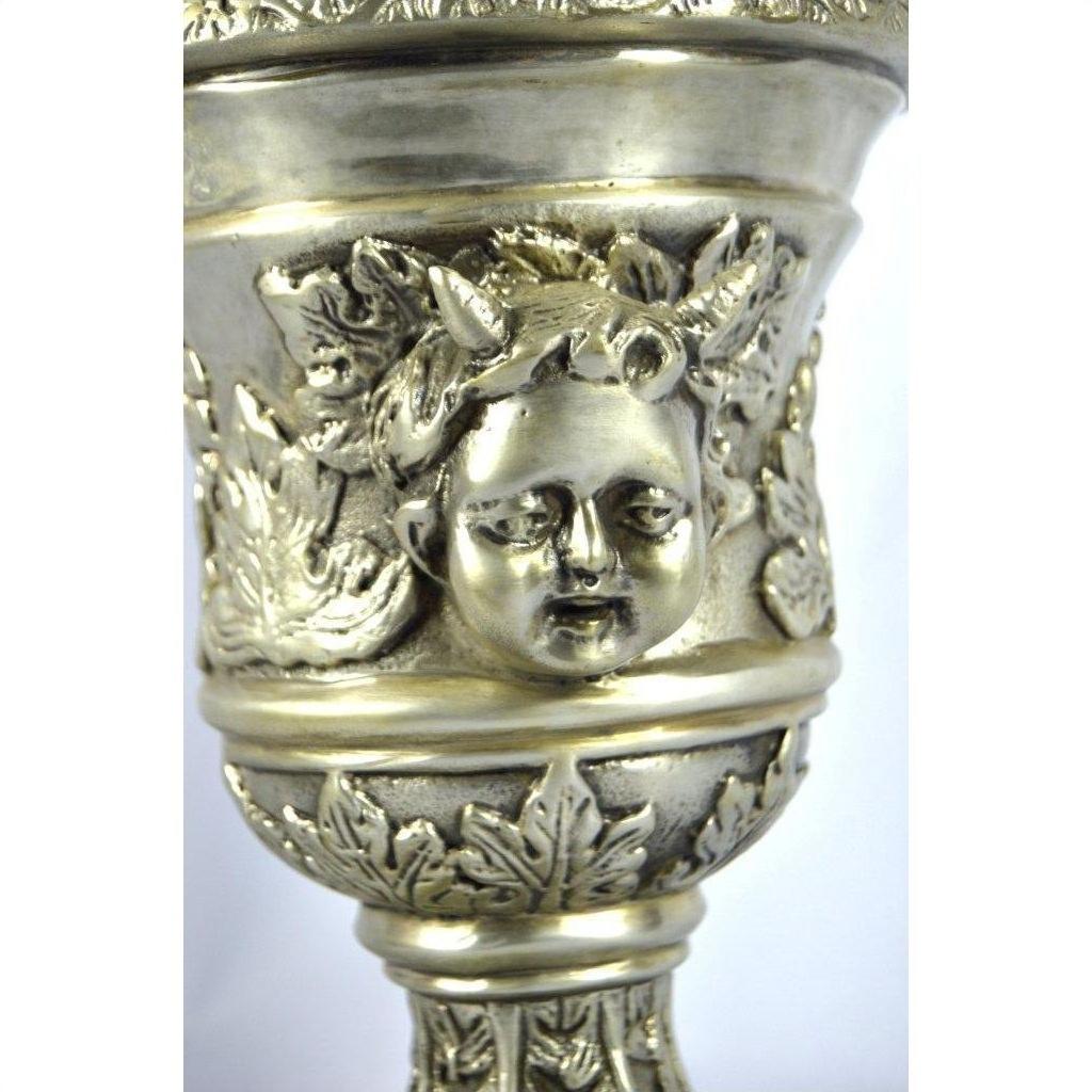 Silver plate urn with figural cherubs and decorative leaf patterns, close-up of bowl details.